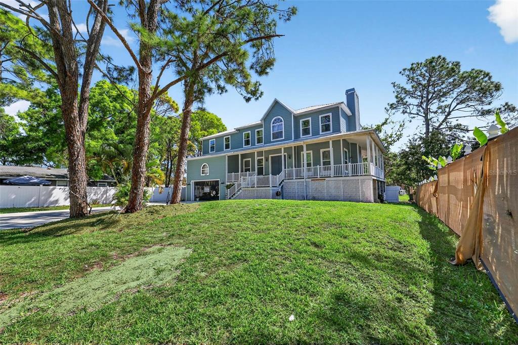 A two-story blue house with a wrap-around porch stands on a grassy lot with trees — 4433 SWEETWATER DRIVE, TAMPA, FL