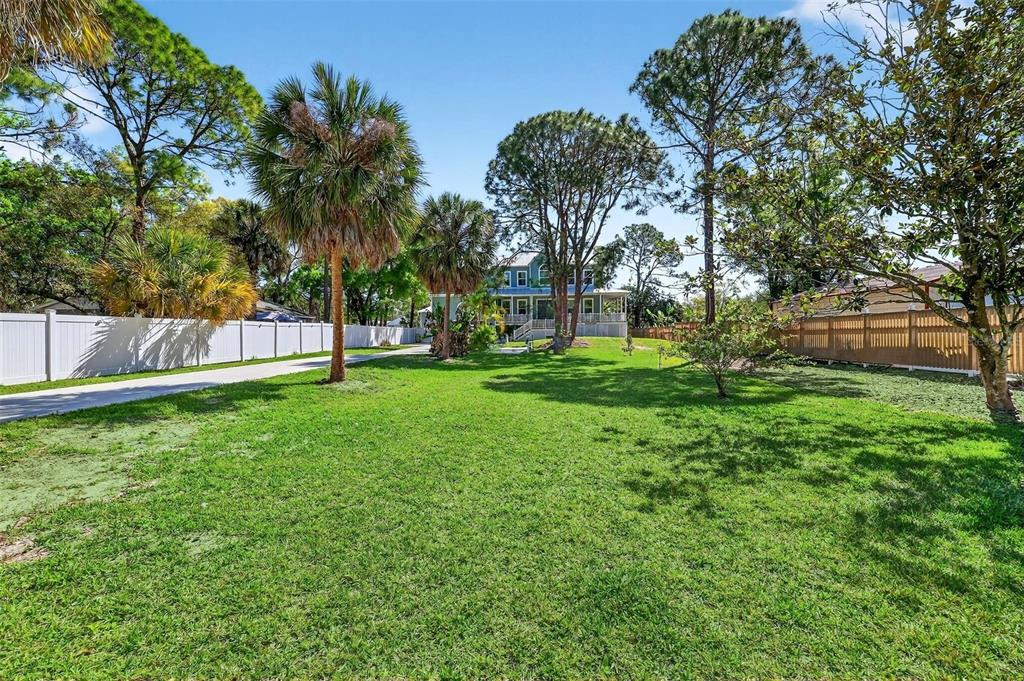 A large grassy yard leads to a blue multi-story house surrounded by trees and fences — 4433 SWEETWATER DRIVE, TAMPA, FL