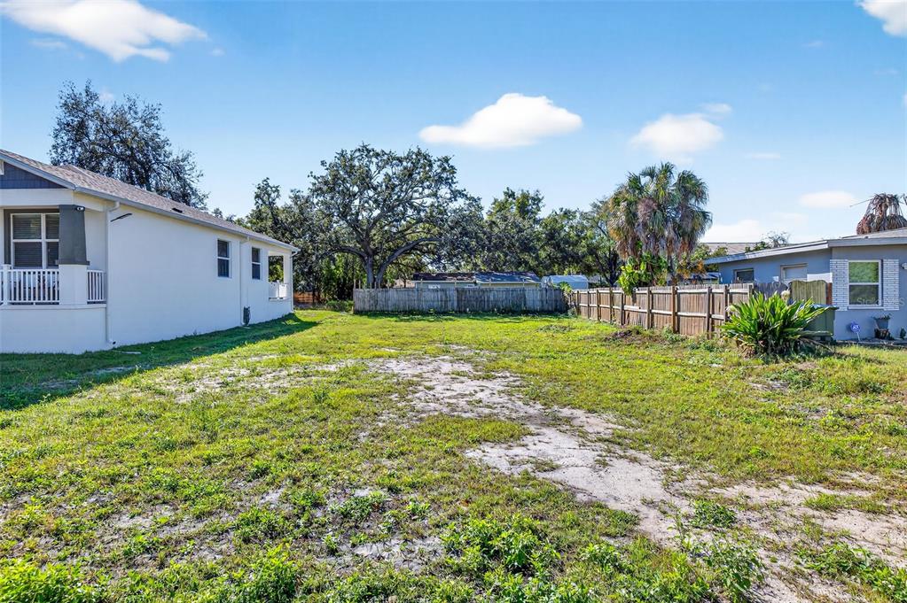 A grassy, vacant residential lot sits between two houses with a wooden fence in back — 3242 ROXBOROUGH AVENUE, CLEARWATER, FL