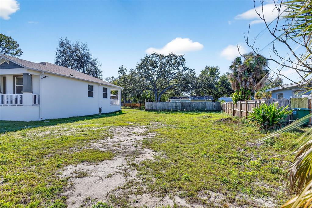 A side view of a white house with a large, grassy, partially dirt backyard — 3242 ROXBOROUGH AVENUE, CLEARWATER, FL