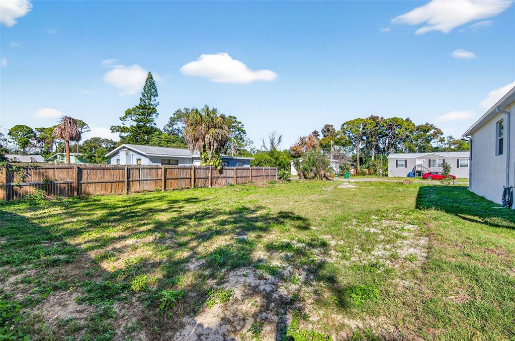 A grassy backyard features a wooden fence and neighboring houses under a blue sky — 3242 ROXBOROUGH AVENUE, CLEARWATER, FL
