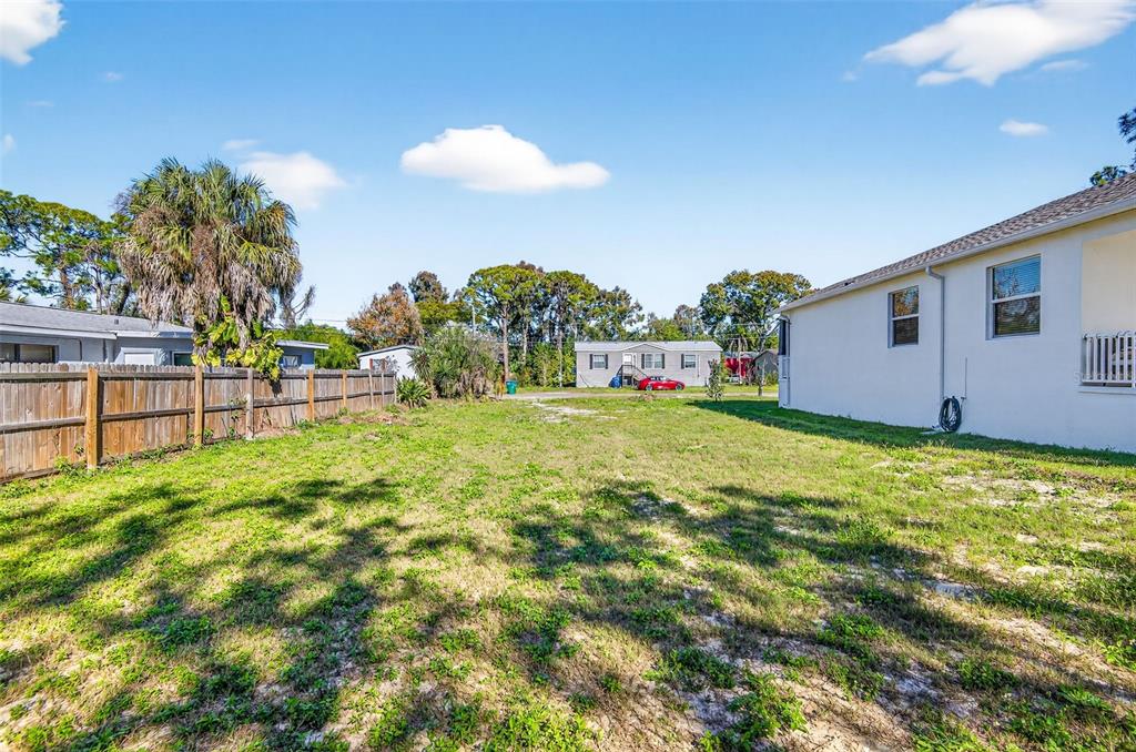 A grassy backyard sits between a wooden fence and the side of a white house — 3242 ROXBOROUGH AVENUE, CLEARWATER, FL