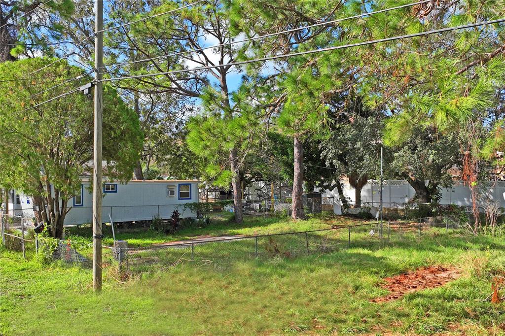 A white mobile home sits on a grassy lot behind a chain-link fence and trees — 5635 VAN DOREN AVE, NEW PORT RICHEY, FL