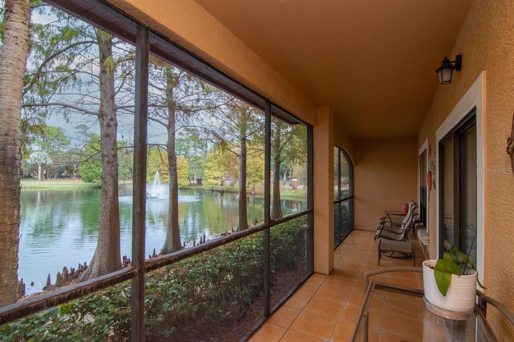 A screened-in porch with tile flooring overlooks a pond with a fountain and trees — 2217 TUSCANY TRACE UNIT 10, PALM HARBOR, FL