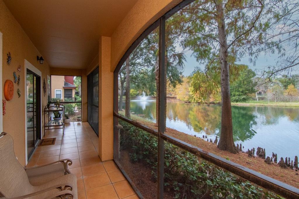 A screened-in patio with tile flooring overlooks a pond with a fountain and trees — 2217 TUSCANY TRACE UNIT 10, PALM HARBOR, FL