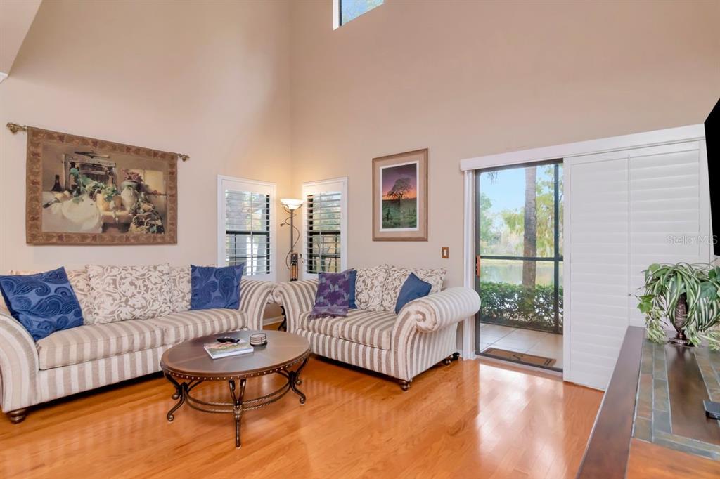 A living room with high ceilings, striped sofas, hardwood floors, and a sliding glass door — 2217 TUSCANY TRACE UNIT 10, PALM HARBOR, FL