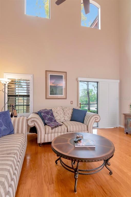A living room features a striped sofa, a round coffee table, and high vaulted ceilings — 2217 TUSCANY TRACE UNIT 10, PALM HARBOR, FL