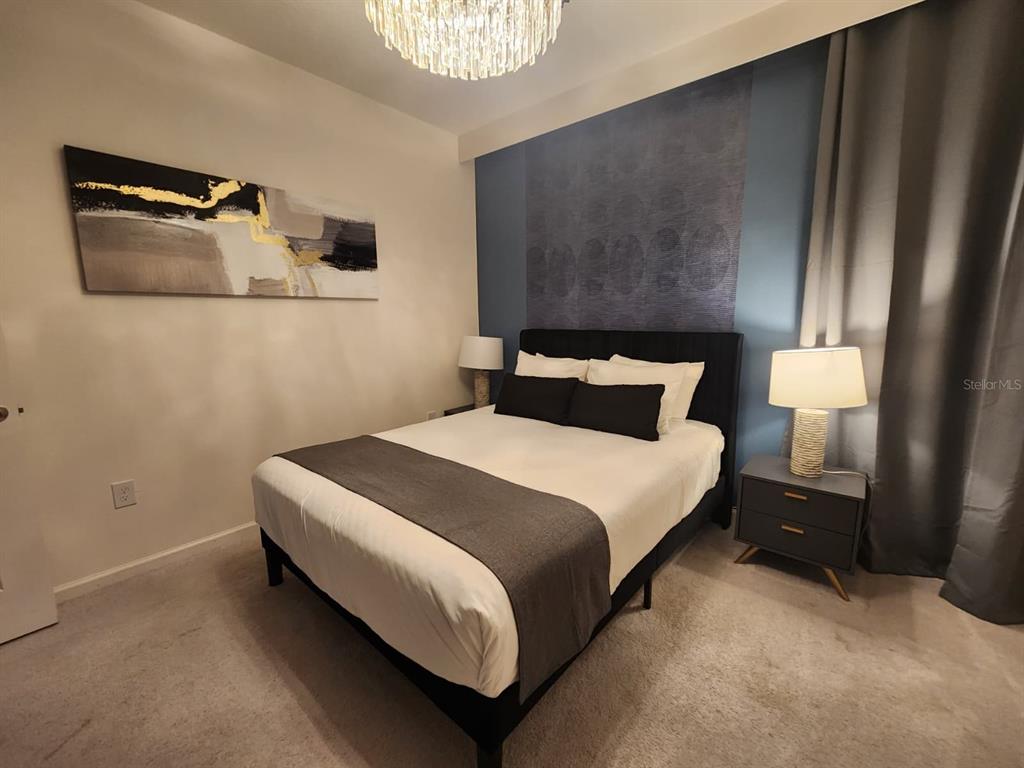 A bedroom features a bed with a dark headboard, a blue accent wall, and chandelier — 4468 MONADO DRIVE, KISSIMMEE, FL