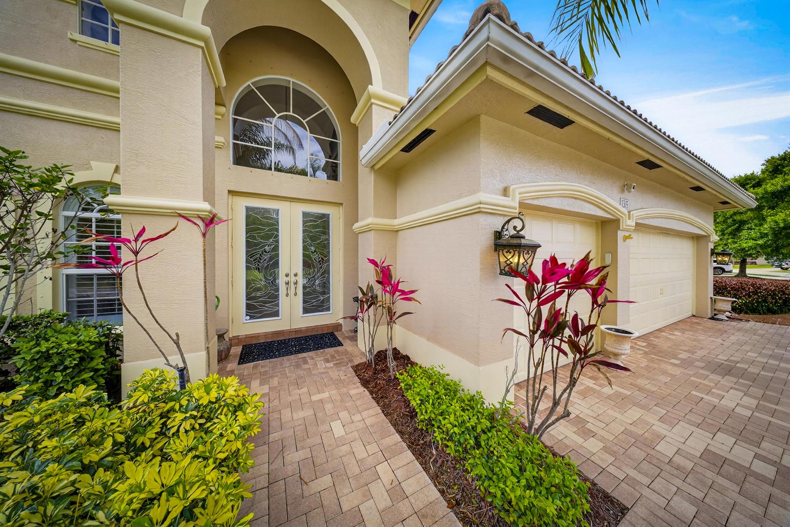 A beige two-story house features a double front door, arched window, and paver driveway — 1315 SE Conference Circle, Stuart FL 34997, STUART, FL
