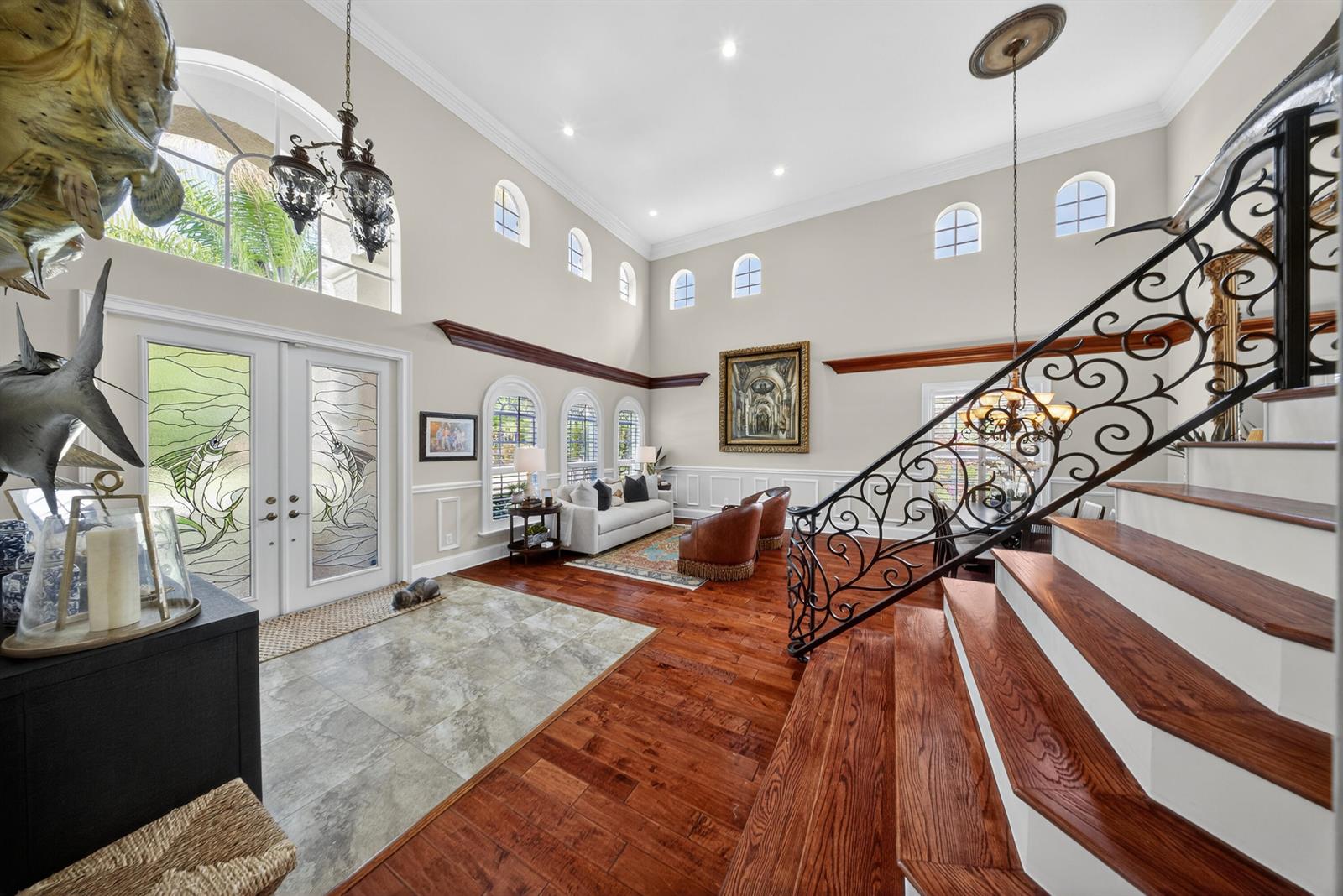 A high-ceilinged foyer features a grand staircase, stained glass doors, and hardwood flooring — 1315 SE Conference Circle, Stuart FL 34997, STUART, FL