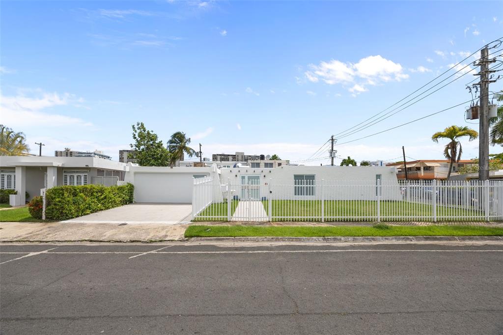 A white, single-story house with a garage and a fenced front yard under a blue sky — 2 CALLE MAR DE IRLANDA, CAROLINA, PR