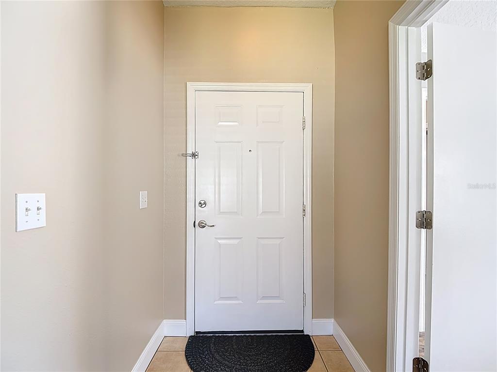 An interior entryway features a white front door with a security bar and tile flooring — 11205 COREY PAVIN LANE, SAN ANTONIO, FL