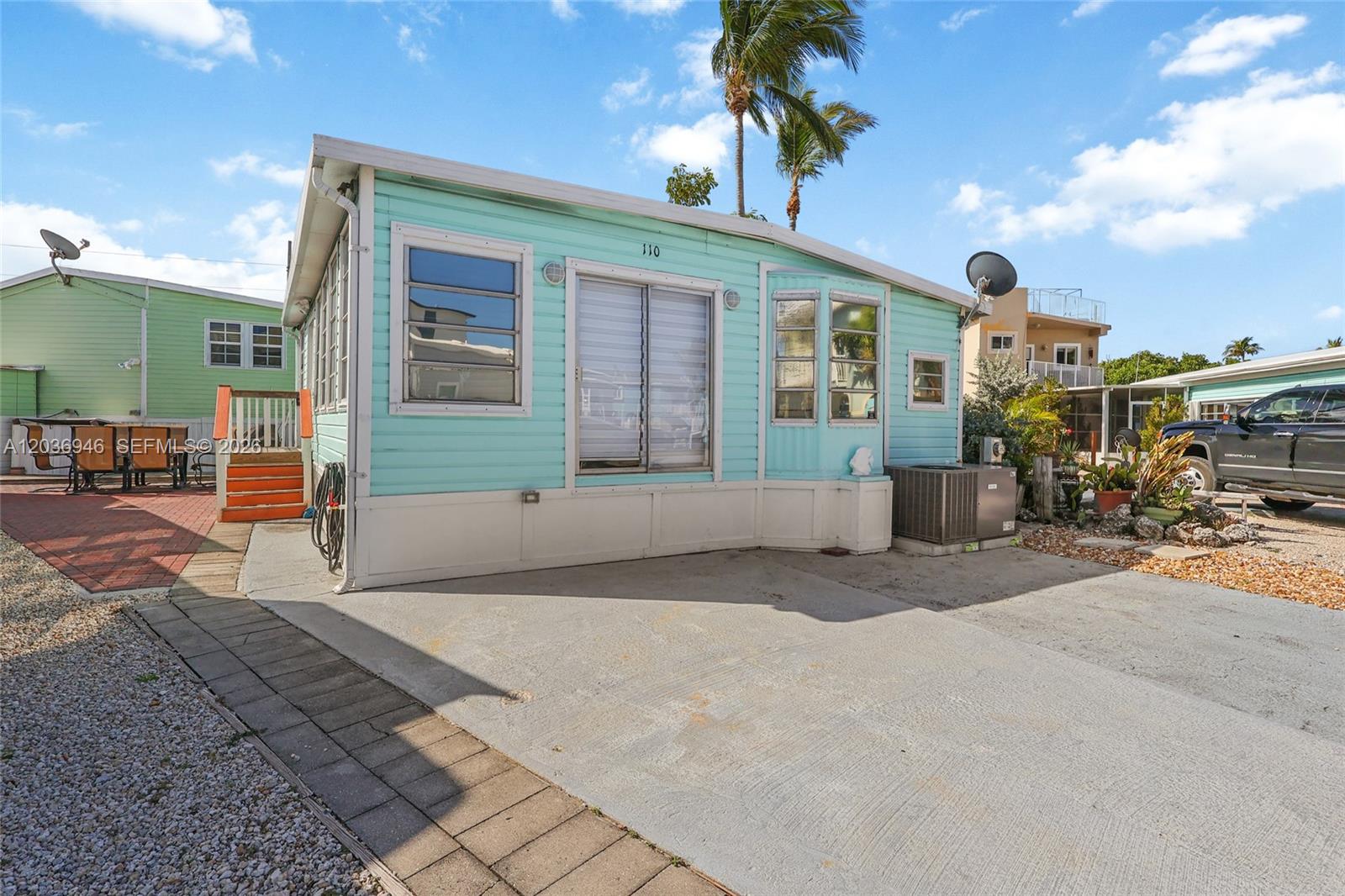 A light blue mobile home with a concrete driveway and a small wooden deck — 65821 OVERSEAS HIGHWAY Unit 110 # 110, Long Key FL 33001, LONG KEY, FL