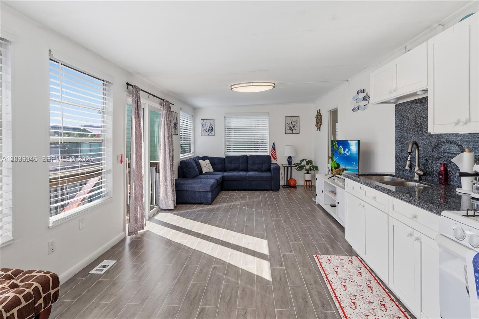 This open-concept living room and kitchen features white cabinetry, dark countertops, and wood-look flooring — 65821 OVERSEAS HIGHWAY Unit 110 # 110, Long Key FL 33001, LONG KEY, FL