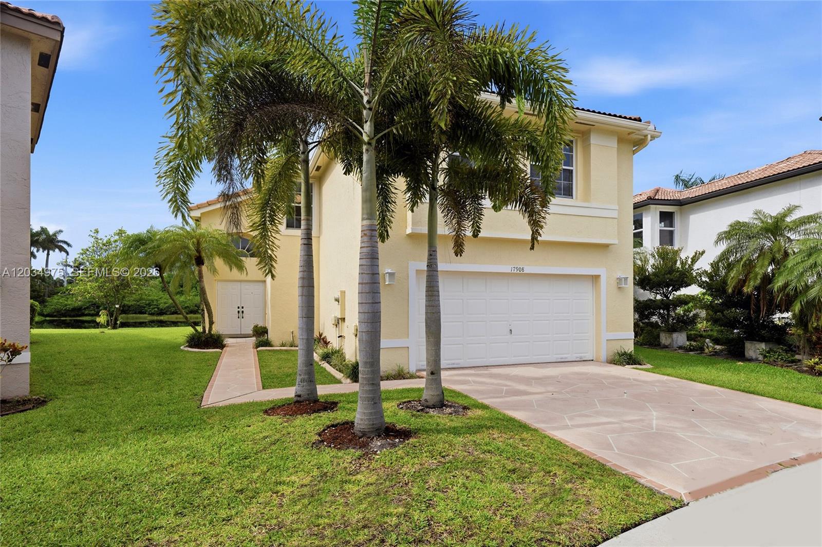 A two-story yellow house features a white garage door, palm trees, and a paved walkway — 17908 SW 30th Ct, Miramar FL 33029, MIRAMAR, FL