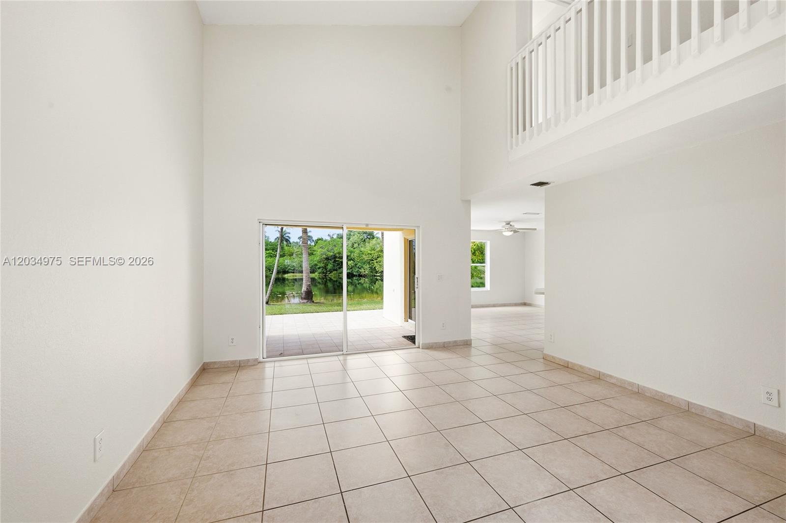 A bright living room features high ceilings, tile flooring, and sliding doors overlooking a lake — 17908 SW 30th Ct, Miramar FL 33029, MIRAMAR, FL