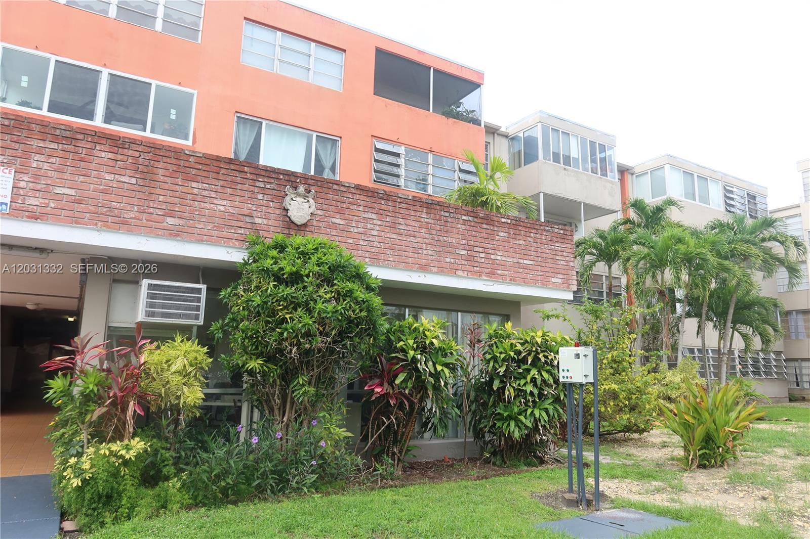 The exterior of a multi-story apartment building features a brick facade, orange stucco, and landscaping — 1850 NE 169th St # 312, North Miami Beach FL 33162, NORTH MIAMI BEACH, FL