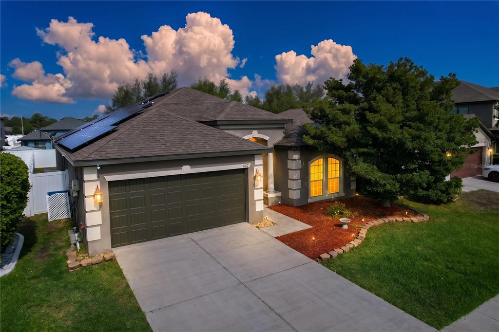 An exterior view of a single-story house with a garage, solar panels, and a tree — 667 HARTFORD HEIGHTS STREET, SPRING HILL, FL