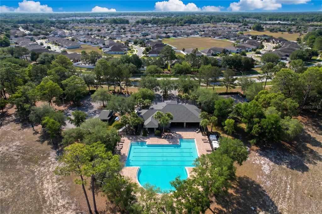 An aerial view shows a community swimming pool and clubhouse surrounded by trees and houses — 667 HARTFORD HEIGHTS STREET, SPRING HILL, FL