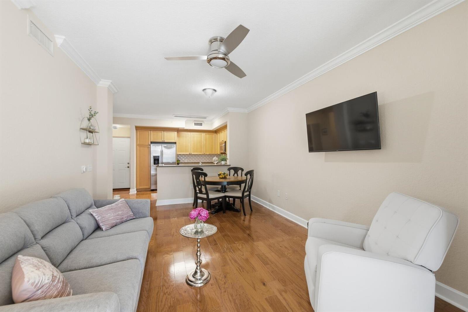 A living room with hardwood floors, a gray sofa, a white armchair, and a dining area — 4 Renaissance Way # 110, Boynton Beach FL 33426, BOYNTON BEACH, FL