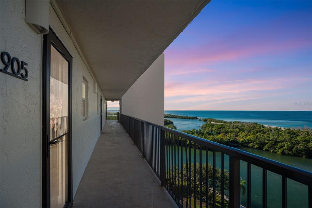 An outdoor walkway with a metal railing overlooks a coastal landscape at sunset — 9397 MIDNIGHT PASS ROAD UNIT 905, SARASOTA, FL