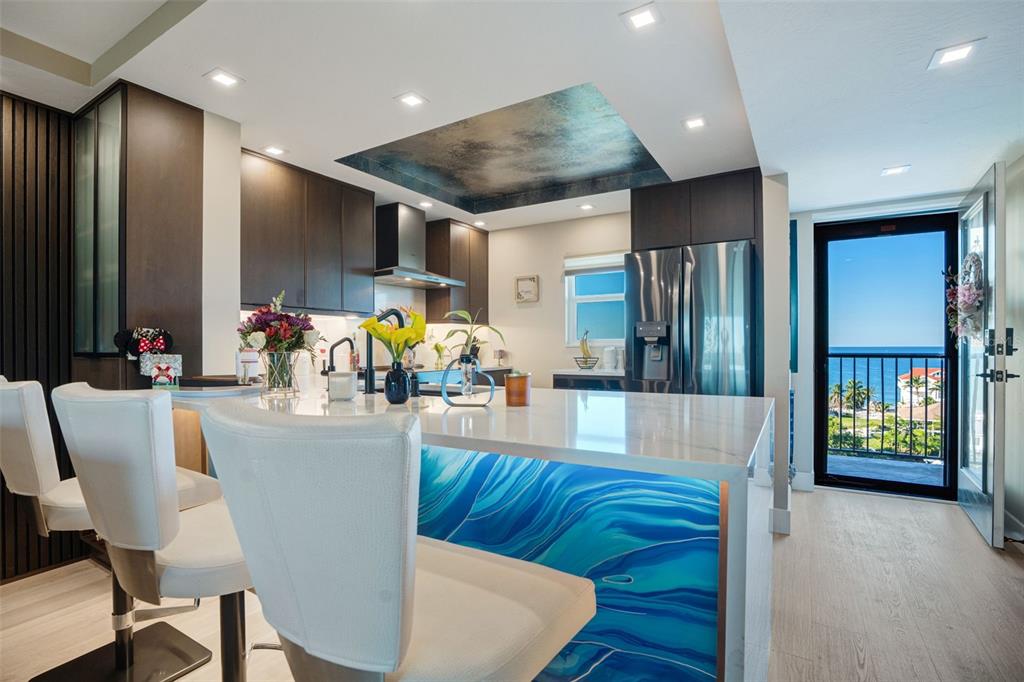 A modern kitchen features a blue wave-patterned island, dark cabinetry, and a view of the ocean — 9397 MIDNIGHT PASS ROAD UNIT 905, SARASOTA, FL