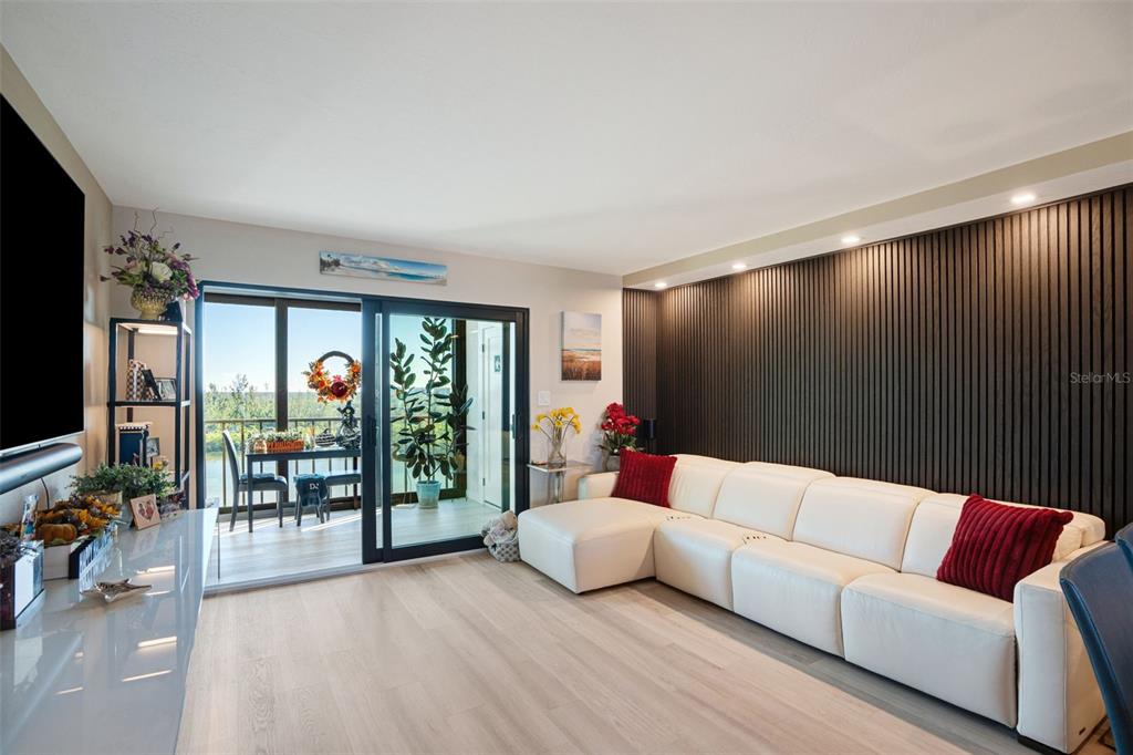 A living room features a white sectional sofa, light wood floors, and a dark slatted wall — 9397 MIDNIGHT PASS ROAD UNIT 905, SARASOTA, FL