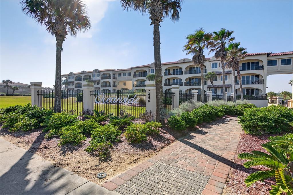 A multi-story residential building with a gated entrance, palm trees, and a brick walkway — 2450 N OCEAN SHORE BOULEVARD UNIT 115, FLAGLER BEACH, FL