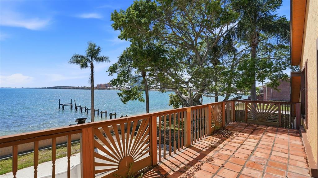A tiled balcony overlooks a waterfront view with trees, a wooden railing, and a dock — 6754 31ST STREET S, ST PETERSBURG, FL