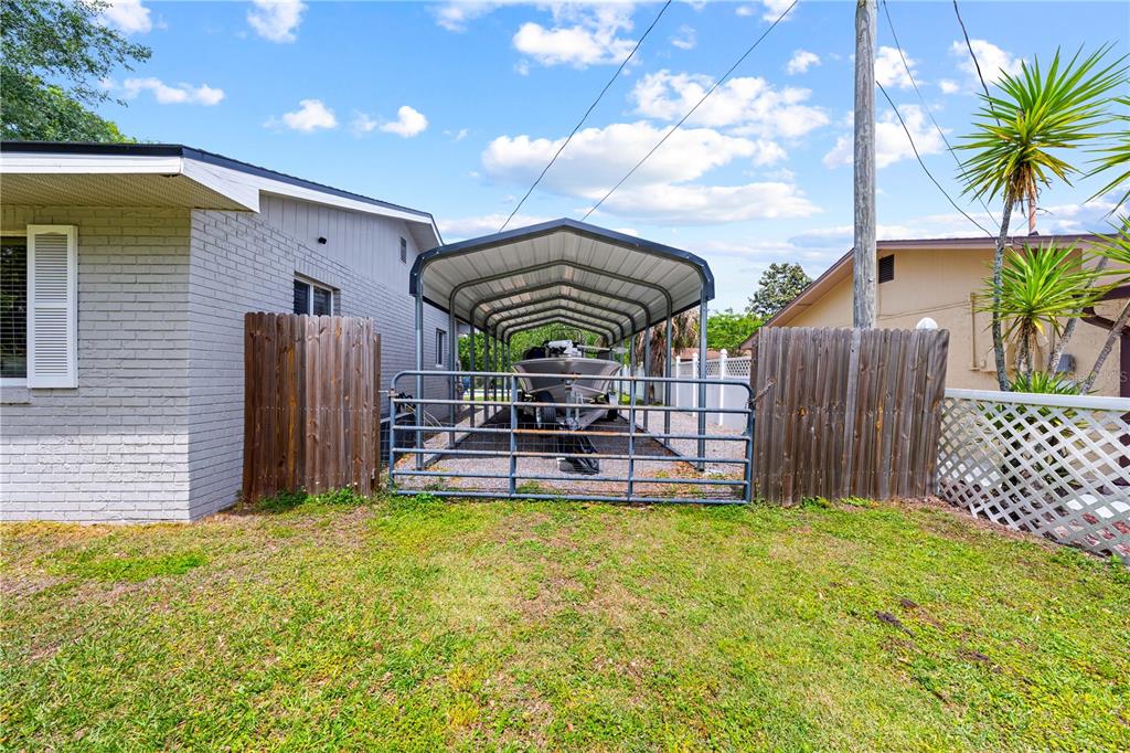 A metal carport housing a boat sits between two houses behind a wooden fence — 6137 BASS HIGHWAY, ST CLOUD, FL