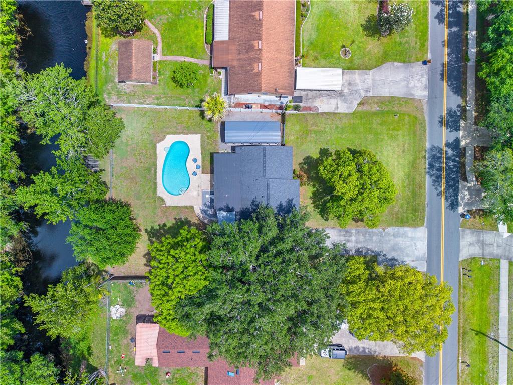 An aerial view shows a house with a swimming pool, large trees, and a canal — 6137 BASS HIGHWAY, ST CLOUD, FL