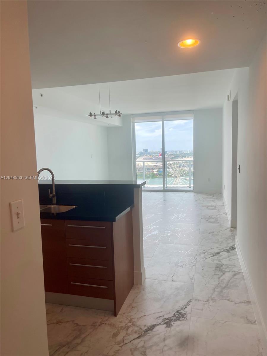 A kitchen with dark cabinets and a sink overlooks a living area with marble floors — 253 NE 2nd St # 2409, Miami FL 33132, MIAMI, FL