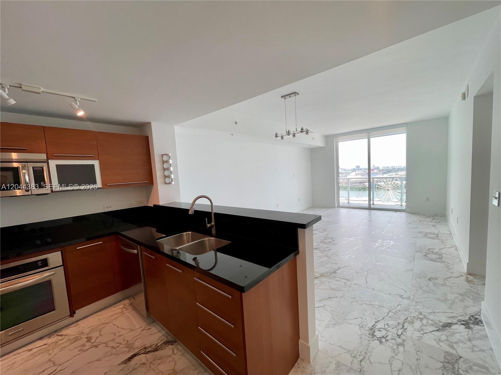 A kitchen with wood cabinets and black countertops overlooks an open living area with marble floors — 253 NE 2nd St # 2409, Miami FL 33132, MIAMI, FL