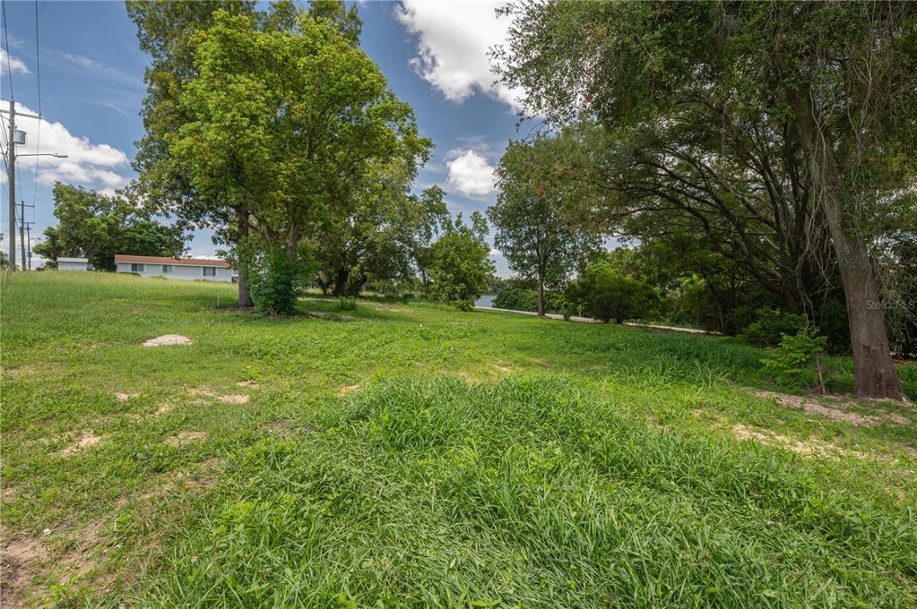 A grassy, sloped lot with several large trees and a view of a distant lake — 504 E MAIN STREET, DUNDEE, FL