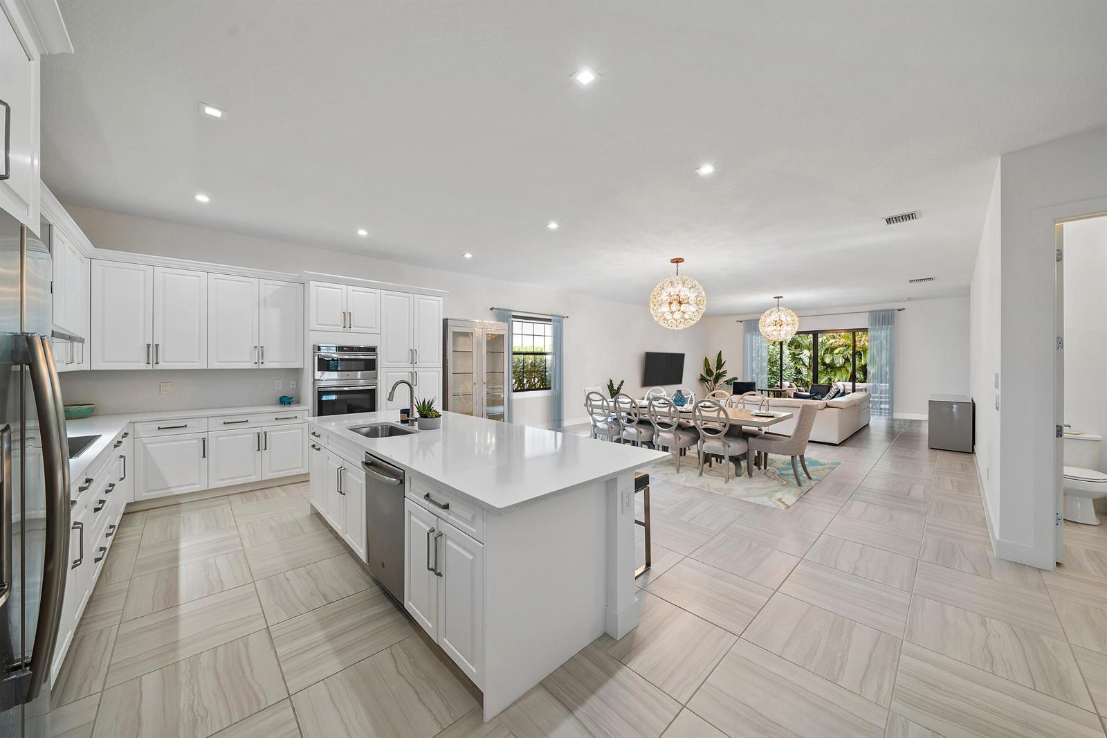 A modern, open-concept kitchen with white cabinetry, a large island, and adjacent dining area — 2938 Gin Berry Way, West Palm Beach FL 33401, WEST PALM BEACH, FL