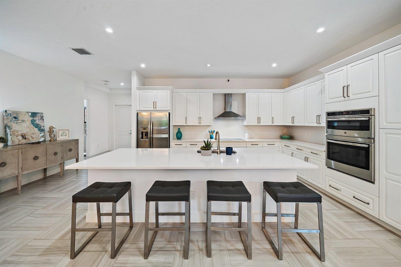 A modern kitchen features white cabinetry, a large central island with bar stools, and stainless appliances — 2938 Gin Berry Way, West Palm Beach FL 33401, WEST PALM BEACH, FL