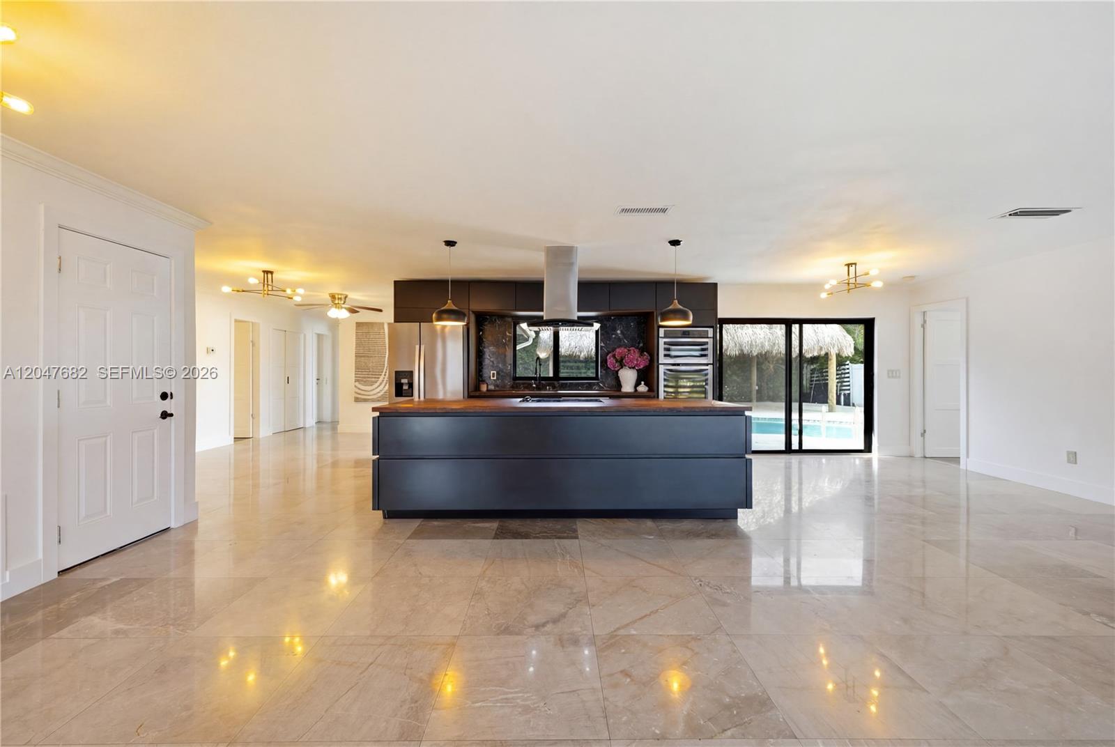 A modern kitchen features a large dark island, wood countertops, and marble tile flooring — BOCA RATON, FL