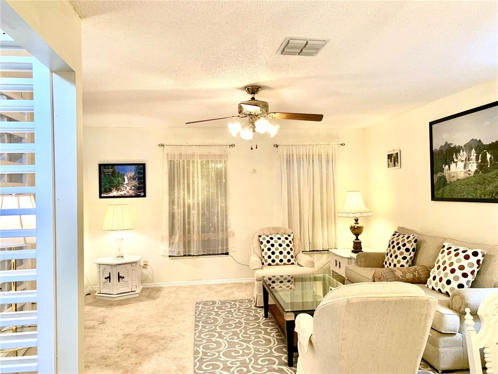 A living room features a ceiling fan, beige carpet, a sofa, and two armchairs — 1891 FORTUNE COURT, DELTONA, FL