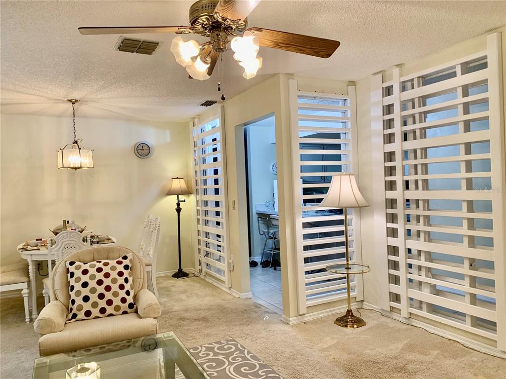 A living room features a ceiling fan, carpeted floors, and white louvered room dividers — 1891 FORTUNE COURT, DELTONA, FL
