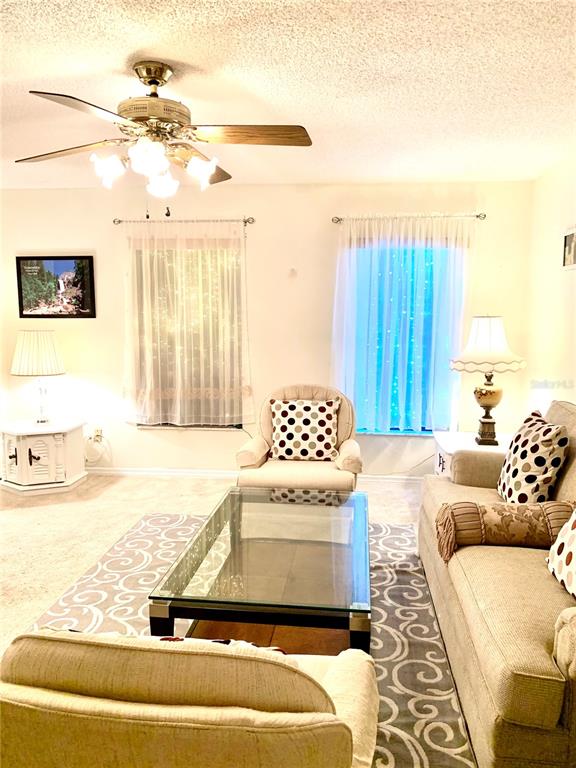 A living room features a ceiling fan, a glass coffee table, and beige upholstered furniture — 1891 FORTUNE COURT, DELTONA, FL