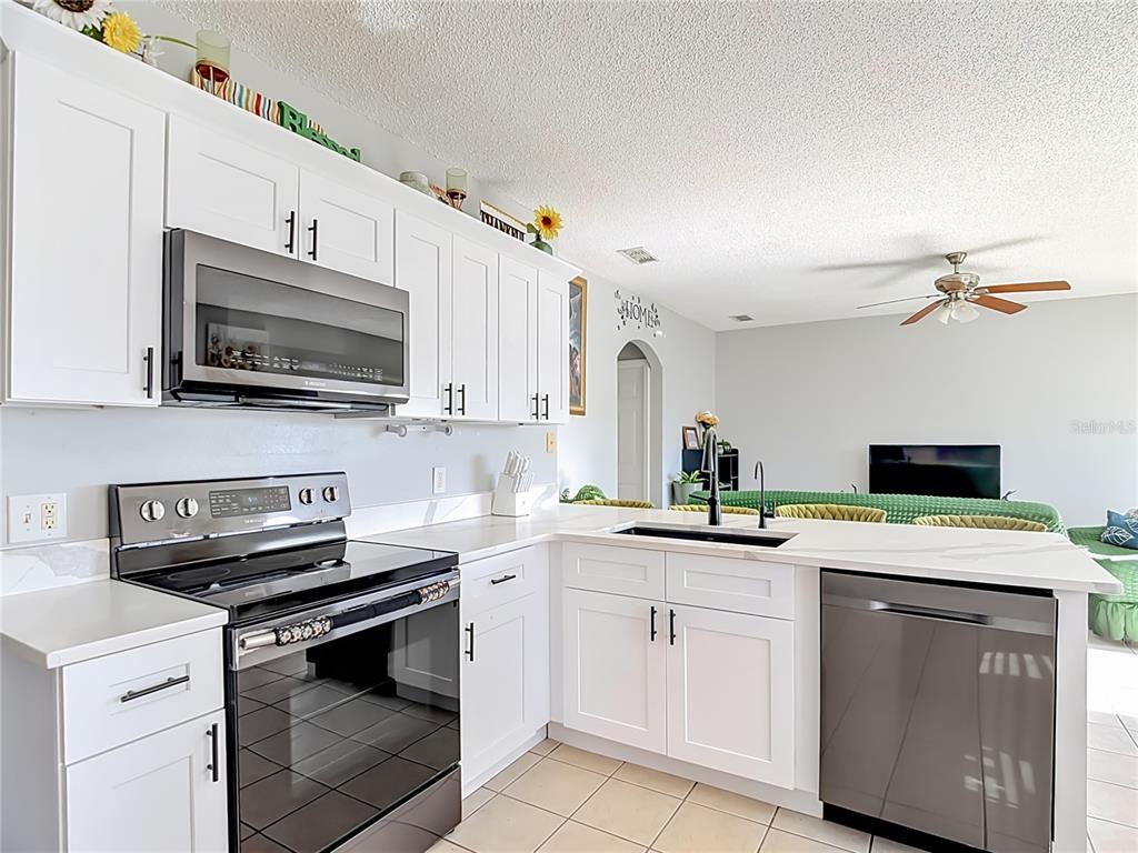 A kitchen with white cabinets, stainless steel appliances, and a peninsula overlooking a living area — 1425 NELSON BROOK WAY, KISSIMMEE, FL