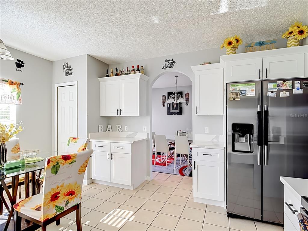 A kitchen with white cabinets, stainless steel appliances, and a dining area with sunflower-patterned chairs — 1425 NELSON BROOK WAY, KISSIMMEE, FL