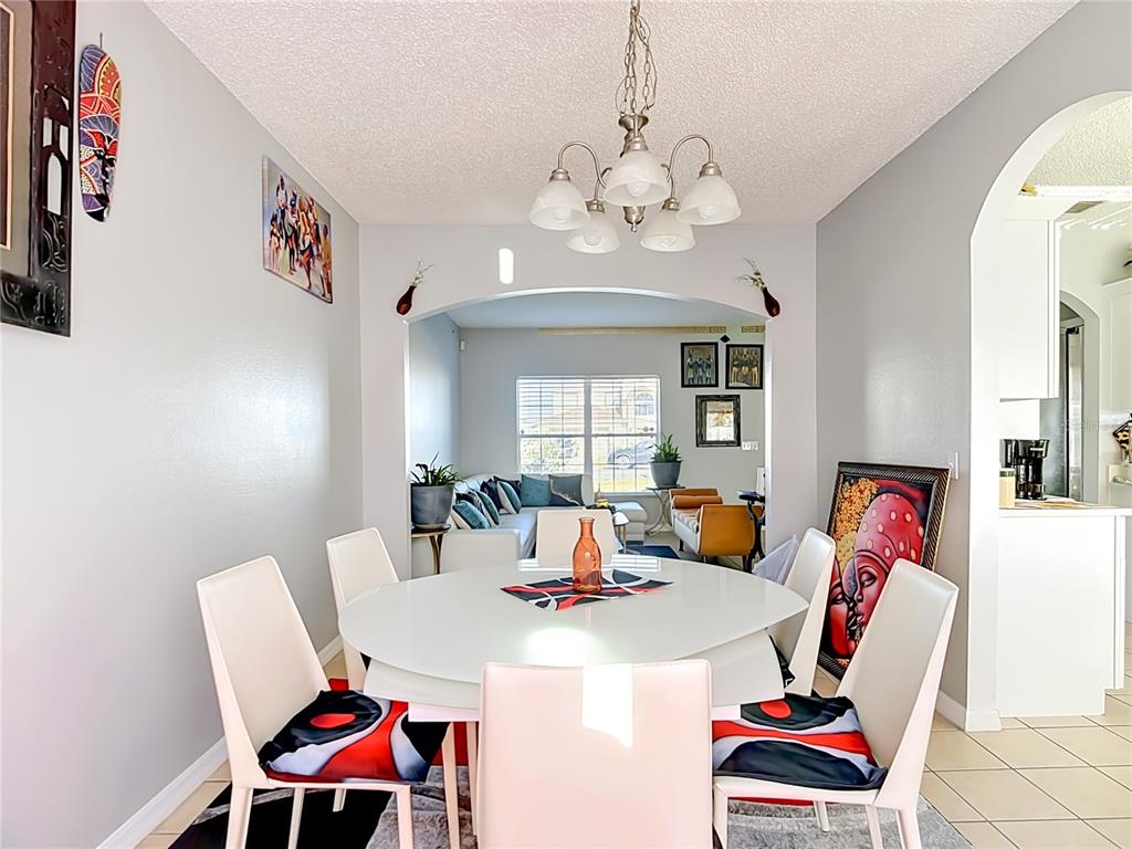 A dining room with a white round table and chairs leads into an adjacent living area — 1425 NELSON BROOK WAY, KISSIMMEE, FL