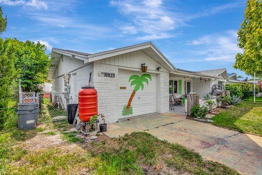 A white brick house features a garage door with a painted palm tree and a driveway — 10825 BRIDLETON ROAD, PORT RICHEY, FL