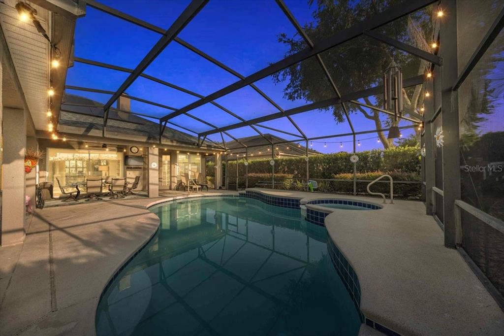 A screened-in patio features a swimming pool, a hot tub, and string lighting at dusk — 9095 LAUREL RIDGE DRIVE, MOUNT DORA, FL
