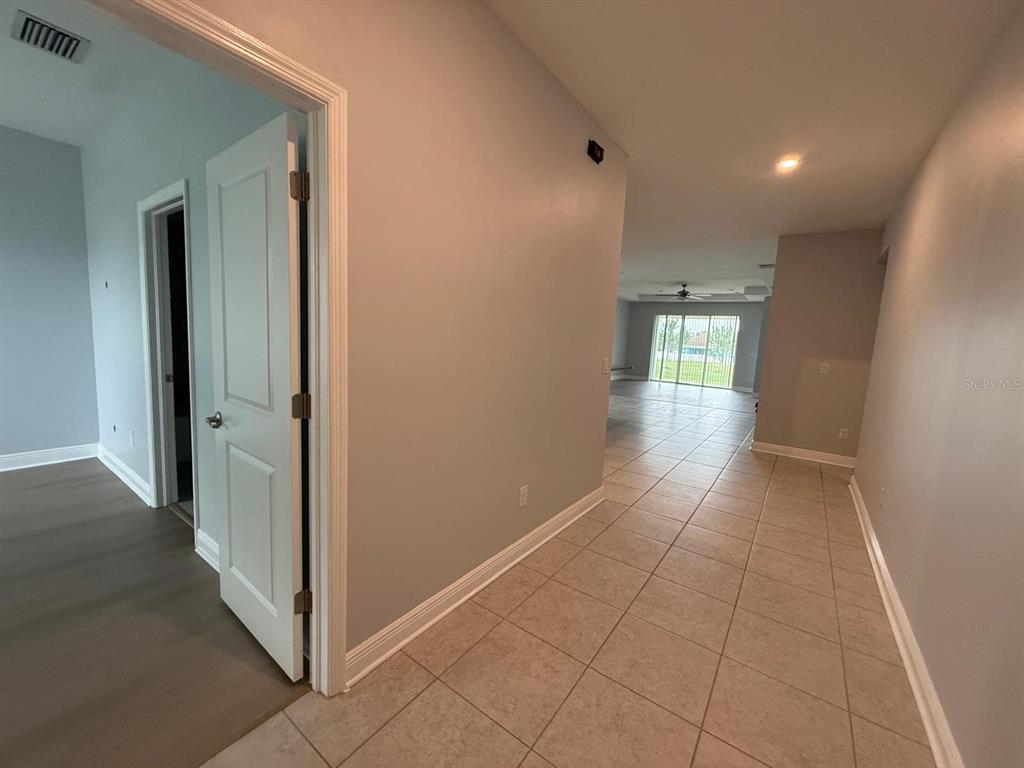 A hallway with tile flooring leads toward an open living area with large glass doors — 34128 EVERGREEN HILL COURT, WESLEY CHAPEL, FL