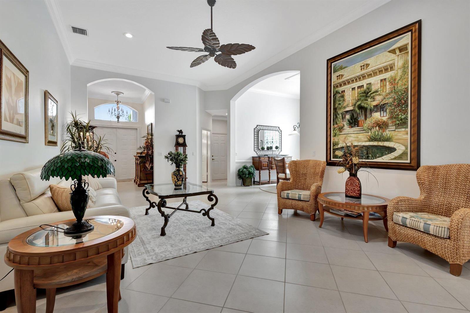A spacious living room features tile floors, wicker armchairs, a white sofa, and arched doorways — 10732 Grande Boulevard, West Palm Beach FL 33412, WEST PALM BEACH, FL