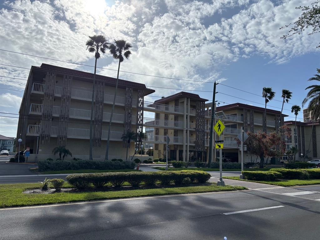 A multi-story apartment building with balconies and palm trees stands beside a paved road — 121 ISLAND WAY UNIT 331, CLEARWATER BEACH, FL