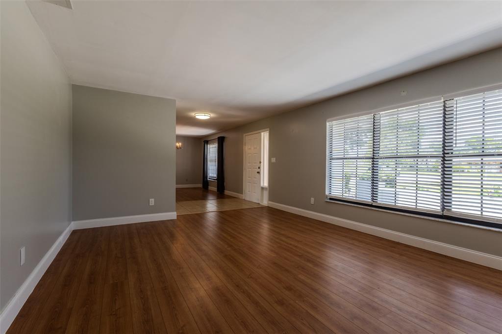 An empty living room features gray walls, wood-look flooring, and a large window with blinds — 1861 CROWLEY CIRCLE E, LONGWOOD, FL