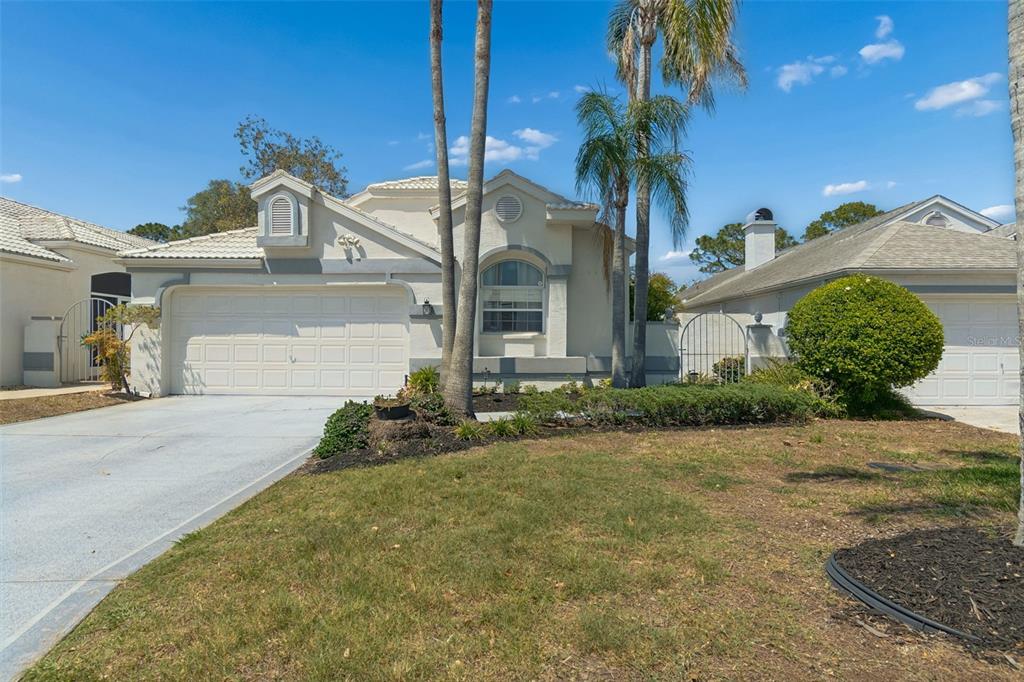 A single-story house with a white stucco exterior, a two-car garage, and palm trees — 10491 CASA GRANDE CIRCLE, SPRING HILL, FL